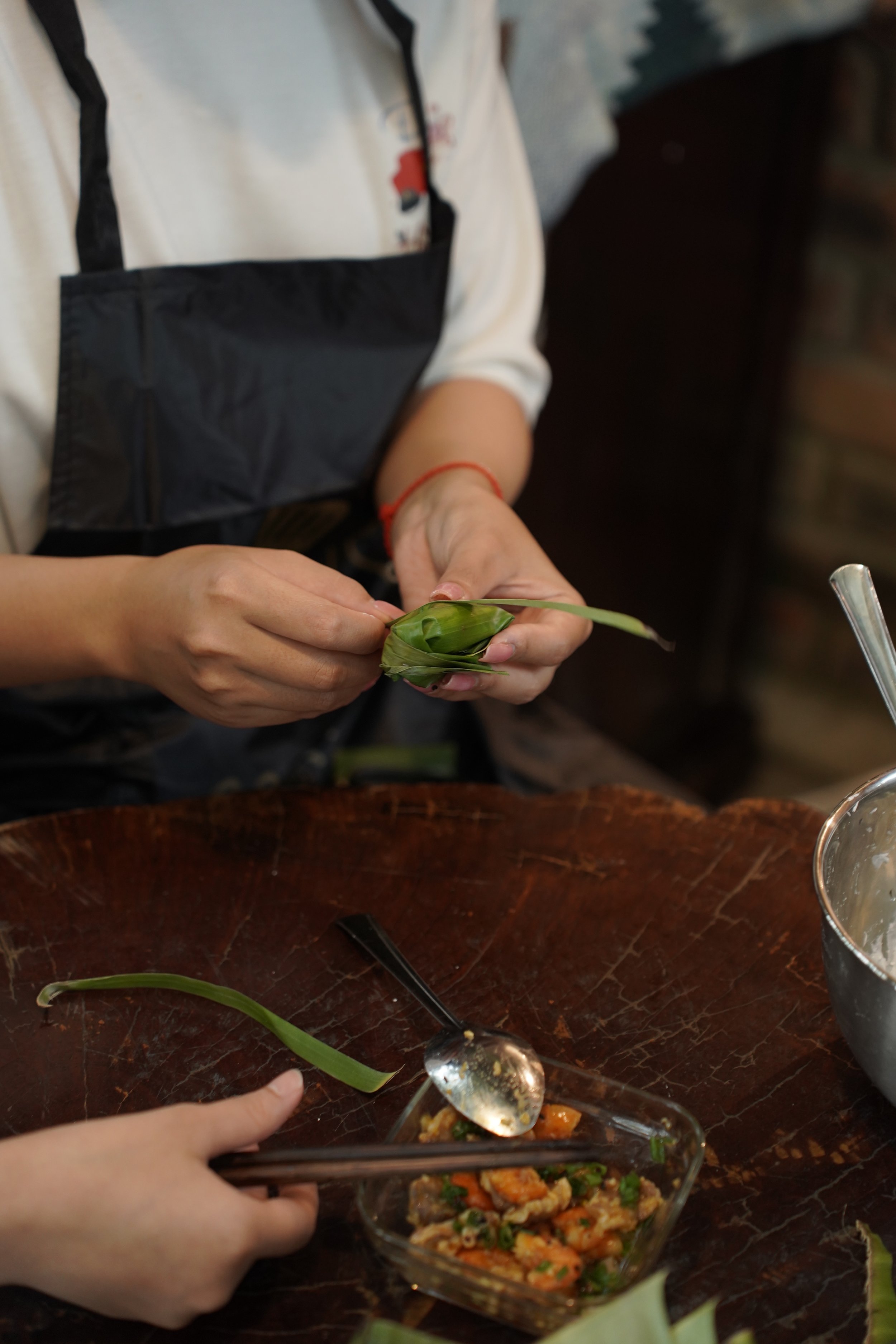 Hands folding a dumpling in a banana leaf.